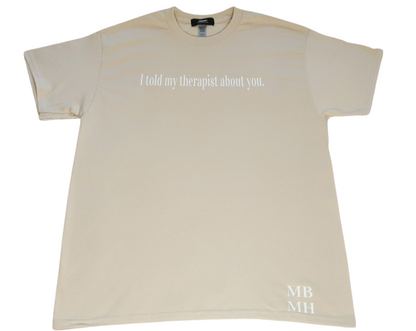 Short sleeve sand colored t-shirt with white vinyl lettering with phrase “I told my therapist about you.”